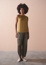 Woman wearing a gold satin top and green satin trousers against a beige wall