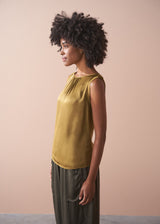 Woman wearing a gold satin top and green satin trousers against a beige wall