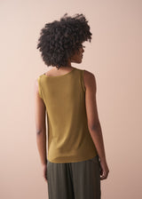 Woman wearing a gold satin top and green satin trousers against a beige wall