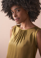 Woman wearing an olive yellow satin sleeveless top against a beige background