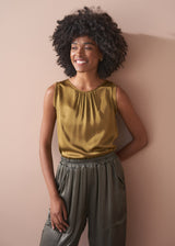 Woman wearing a gold satin top and green satin trousers against a beige wall