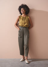 Woman wearing a gold satin top and green satin trousers against a beige wall