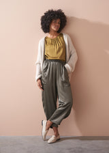Woman wearing a gold satin top and green satin trousers against a beige wall