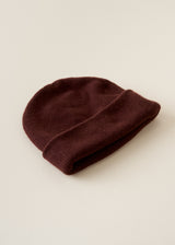 A folded knit beanie hat in a deep burgundy or maroon color, displayed on a clean, light beige background.