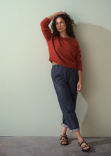 Woman wearing a red sweater and blue jeans against a plain wall.