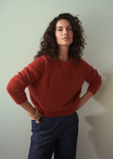 Woman wearing a red sweater and dark jeans against a plain background