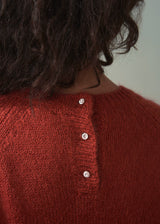 Close-up of a person wearing a red knitted sweater with buttons on a plain background