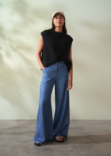 Woman wearing a black sleeveless knit sweater and blue jeans against a neutral background