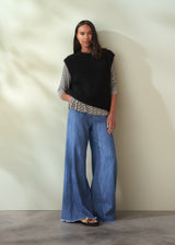 Woman wearing a black sleeveless knit sweater and blue jeans against a neutral background