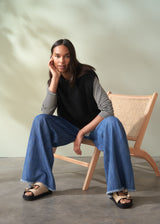 Woman wearing a black sleeveless knit sweater and blue jeans against a neutral background