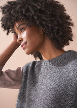 Woman wearing a grey sleeveless sparkle sweater against a beige background
