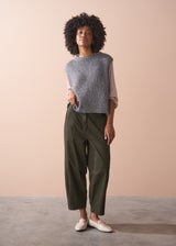 Woman wearing a grey sleeveless sparkle sweater against a beige background