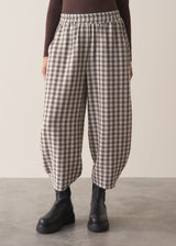 Woman wearing a brown poloneck sweater and checked barrel leg trousers against a plain background