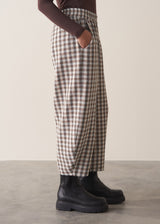 Woman wearing a brown poloneck sweater and checked barrel leg trousers against a plain background