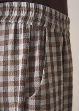 Woman wearing a brown poloneck sweater and checked barrel leg trousers against a plain background