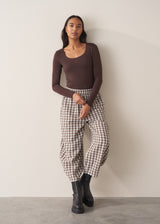 Woman wearing a brown poloneck sweater and checked barrel leg trousers against a plain background