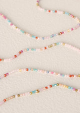 Several strands of small multicolored seed beads arranged in gentle curves on a light beige textured background.