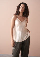 Woman wearing a beige satin camisole top and dark green trousers against a plain background