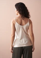 Woman wearing a beige satin camisole top and dark green trousers against a plain background