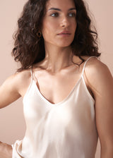 Woman wearing a beige satin camisole top and dark green trousers against a plain background