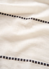 Close-up of a light cream or off-white fabric with a black dotted border pattern running horizontally.