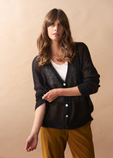 Woman wearing a black cardigan over a white shirt with yellow pants against a beige background