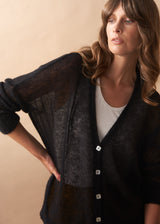 Woman wearing a black cardigan over a white shirt against a beige background