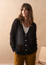 Woman wearing a dark cardigan over a white shirt with yellow pants against a beige background