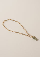 Gold chunky chain necklace with a green stone pendant on a beige background