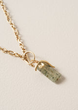 Gold chunky chain necklace with a green stone pendant on a beige background