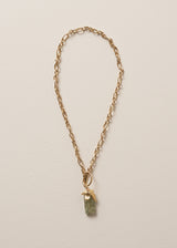 Gold chunky chain necklace with a green stone pendant on a beige background
