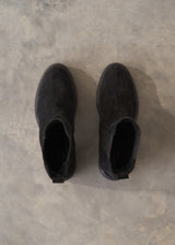 A pair of black suede Chelsea-style ankle boots shown from a top-down view on a textured gray concrete floor.