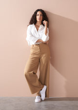 Woman wearing a white shirt and wide leg beige trousers against a beige wall