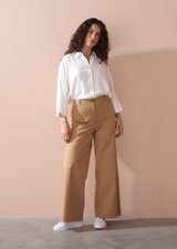 Woman wearing a white shirt and wide leg beige trousers against a beige wall