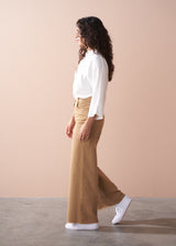Woman wearing a white blouse and tan wide-leg trousers against a beige background