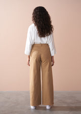 Woman wearing a white blouse and tan wide-leg trousers against a beige wall.