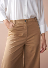 Person wearing a white shirt and wide leg beige trousers against a beige background