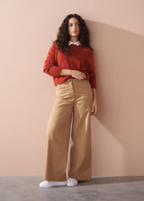 Woman wearing a red sweater and beige wide leg trousers against a beige wall