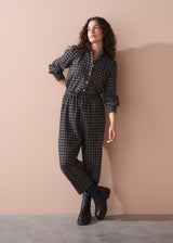 Woman wearing a black and white checkered outfit with barrel leg trousers against a beige wall.