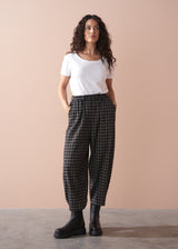 Woman wearing a white t-shirt and plaid barrel leg trousers against a beige background