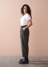 Woman wearing a white t-shirt and checkered barrel leg trousers against a beige background