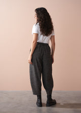 Person wearing checkered barrel leg trousers and a white top against a beige wall