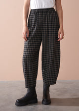 Person wearing black and white checkered barrel leg trousers with a plain background