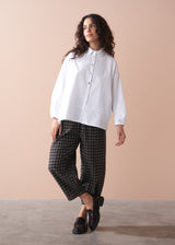 Woman wearing a white shirt and checkered barrel leg trousers against a beige background