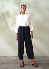 Woman wearing a white shirt and navy corduroy barrel leg trousers against a plain background