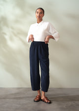 Person wearing a white shirt and navy corduroy barrel leg trousers standing against a plain background