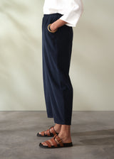 Person wearing navy corduroy barrel leg trousers and white shirt with brown sandals on a neutral background