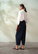 Woman wearing a white blouse and navy corduroy barrel leg trousers against a plain background