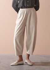 Woman wearing a check shirt and beige corduroy barrel leg trousers against a beige background