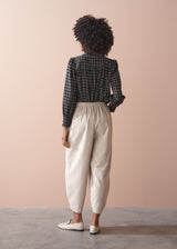 Woman wearing a check shirt and beige corduroy barrel leg trousers against a beige background